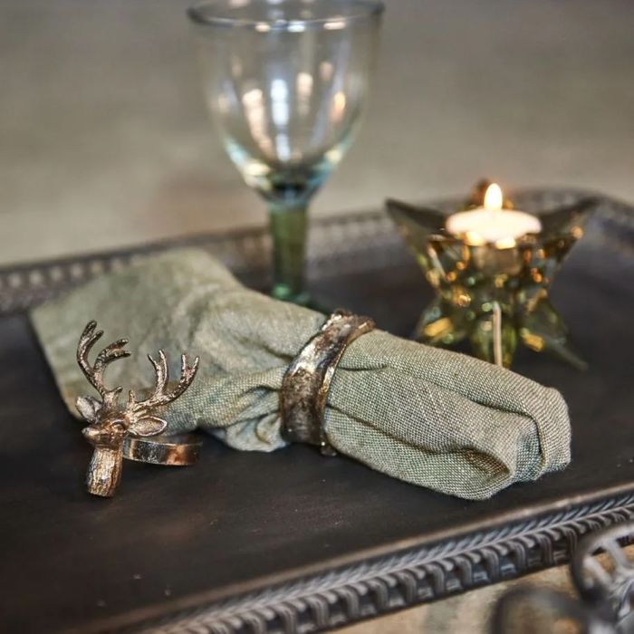 Speedtsberg servietring i antik sølvfarve omkring en rustik stofserviet med levende lys i baggrunden