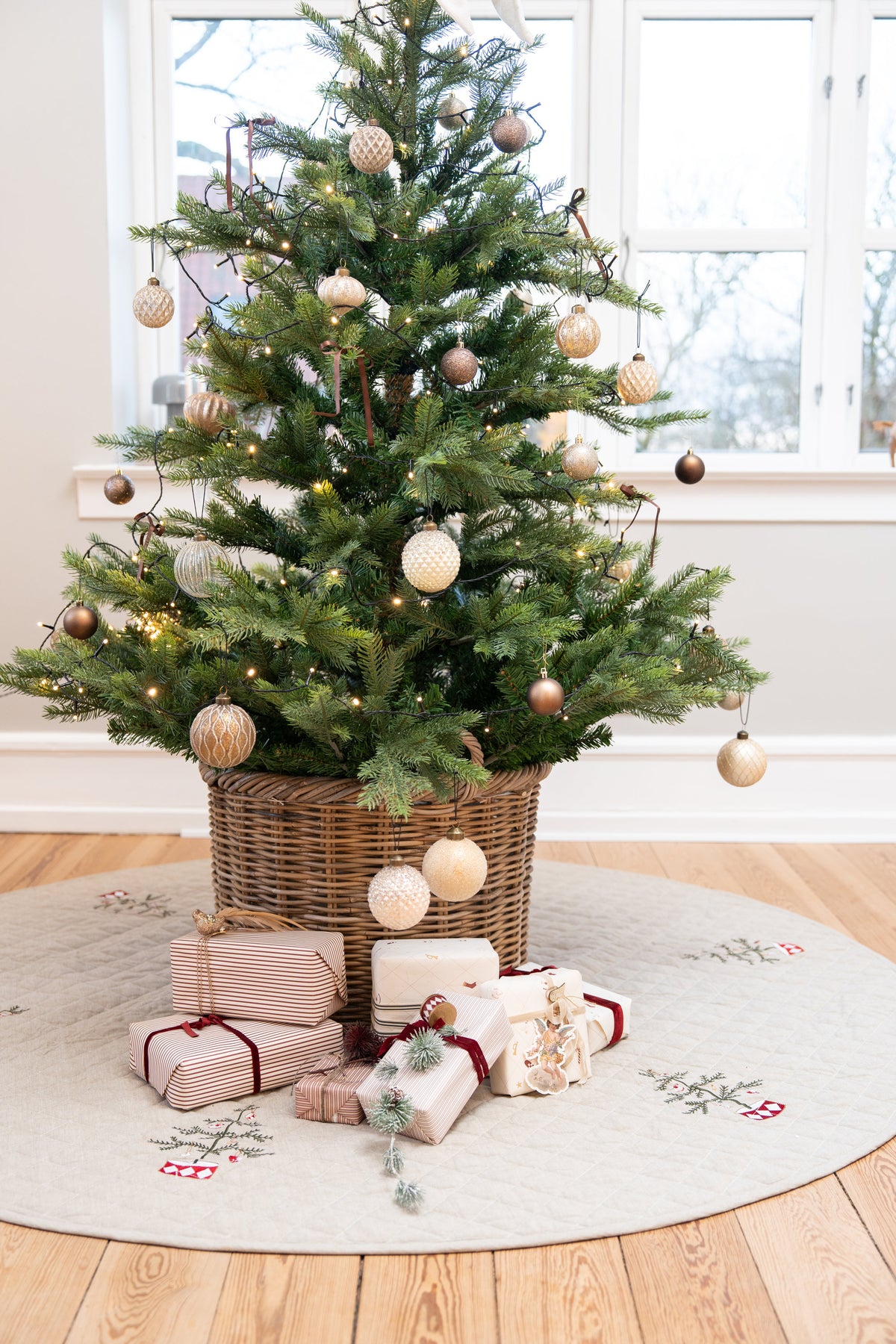 Julgran med pynt i en korg stående på en quiltad julgransmatta med broderi