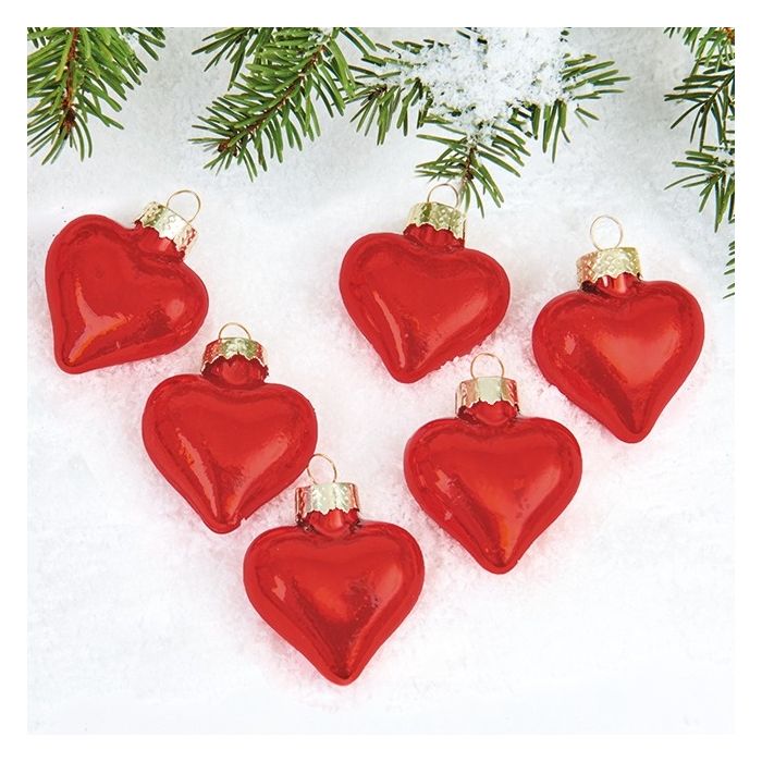 Julehjerter i glas i mat rød liggende på kunstsne med gran.