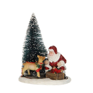 Julemanden er i gang med at pynte op. Julemanden og hans rådyr har øjenkontakt ved siden af det snedækket juletræ. Sød figur fra Luville. 