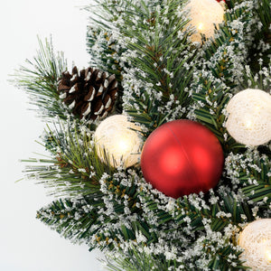 Rød julekugle, kogle og lysende bolde på krans