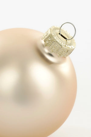 Toppen av en matt cremefärgad julgranskula i glas