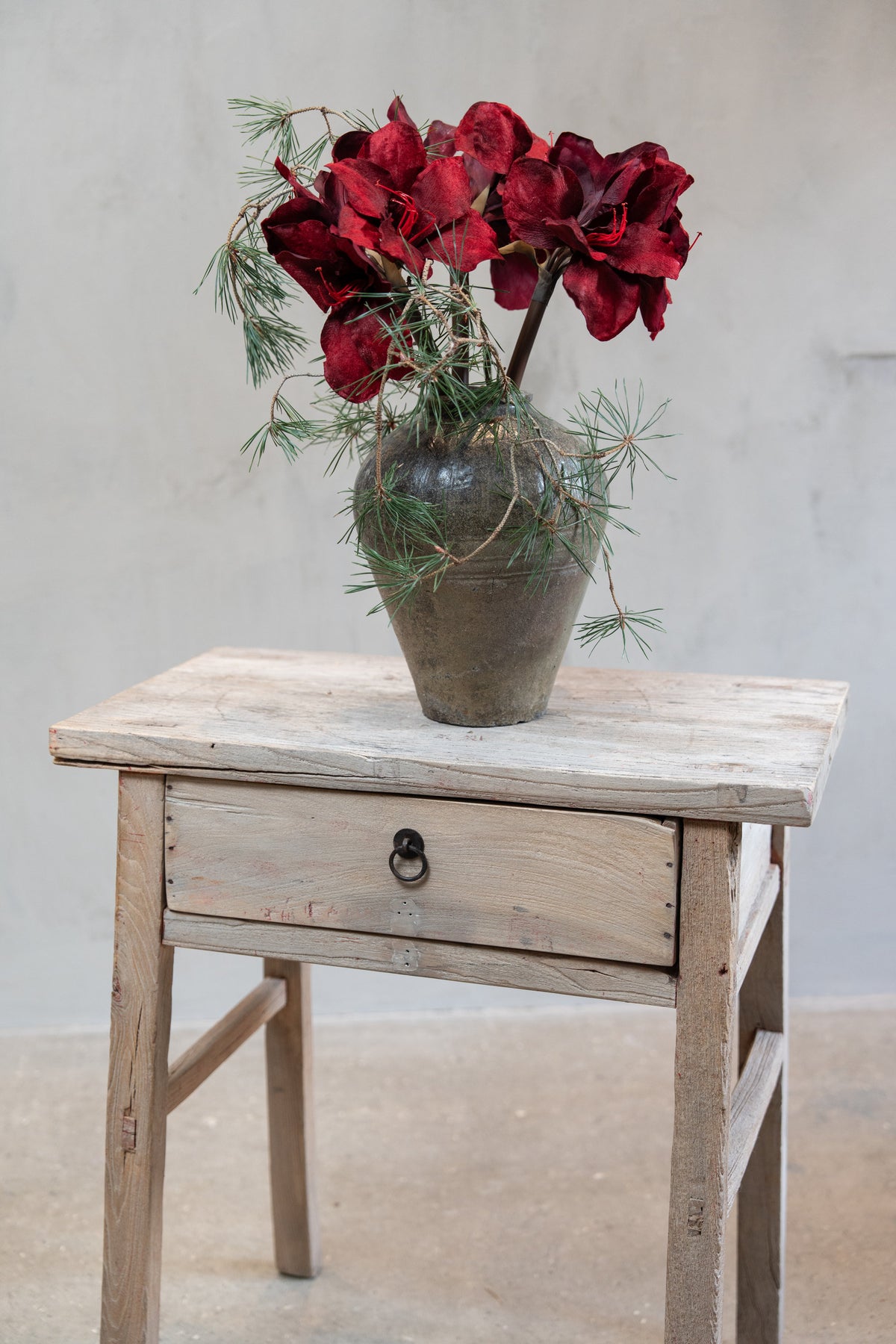 Bukett med konstgjorda stjälkar av amaryllis med vinröda blommor och tallkvistar i vas