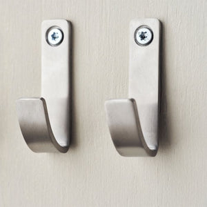 To Meraki knager i børstet stål med sølvfinish hængende på væg