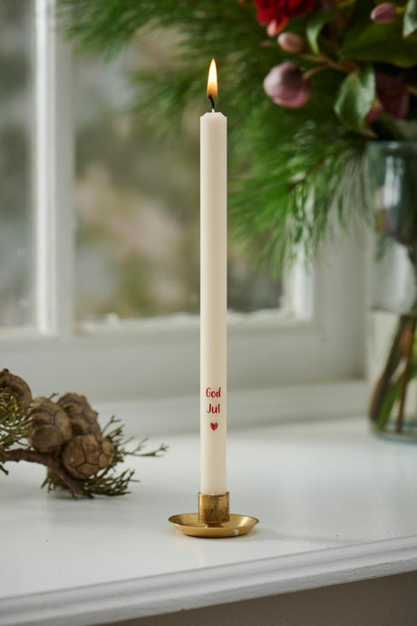 Ljus med texten 'God jul' i en guldfärgad ljusstake på fönsterbrädan