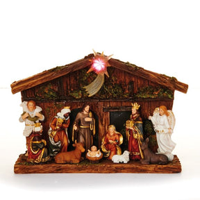 Krybbespil foran flot træagtig bygning med  stjerne på taget med lys i. Til stede er Josef og Jomfru Maria med det lille Jesus barn samt de 3 vise mænd, Kejser Augustus og en smuk engel. Fra Pobra.
