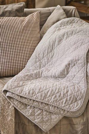 Quilt med hvide og mørkegrå mælkedrengestriber fra Ib Laursen hængende på sofa