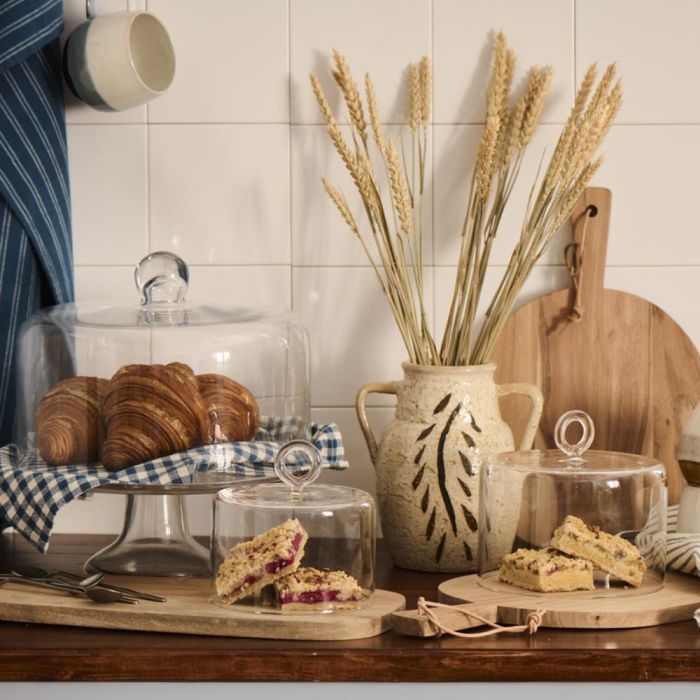 Kagefad i glas på fod fra Ib Laursen med croissanter og blåternet dug under glasklokke med vase på køkkenbord